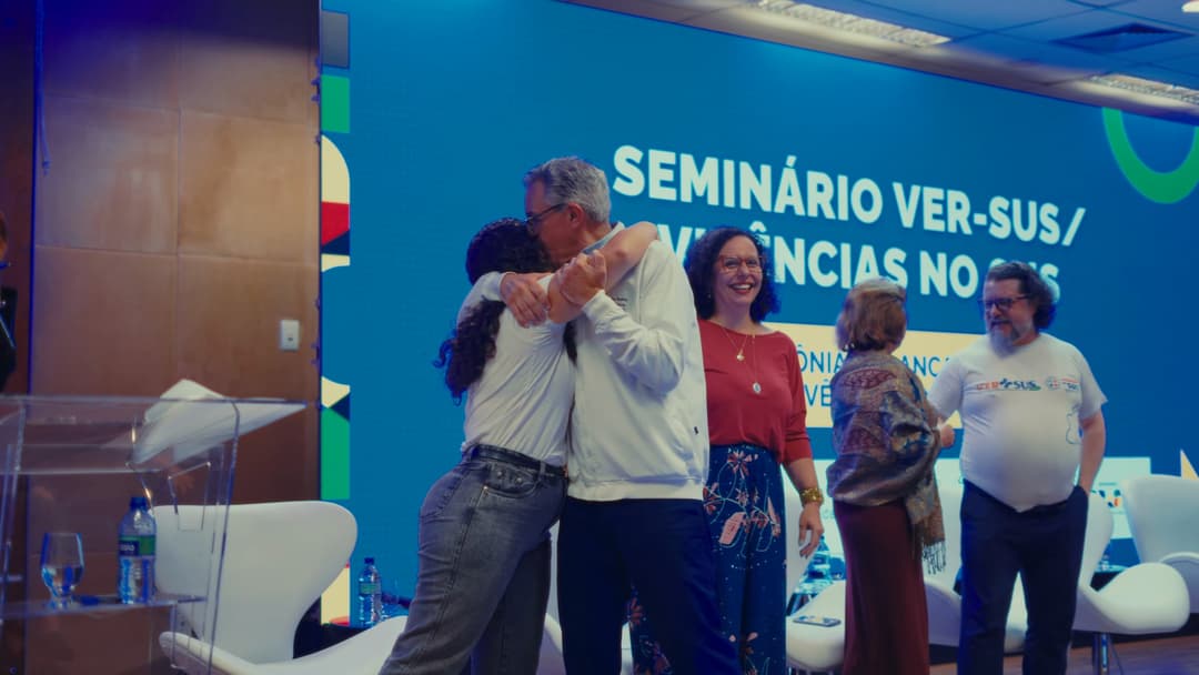 O Ministro da Saúde abraça uma participante no palco enquanto outras pessoas sorriem ao lado.