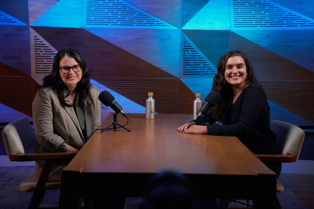 Bianca Orrico e Isabella Ferro sorriem sentadas à mesa do set de videocast do curso da SaferNet