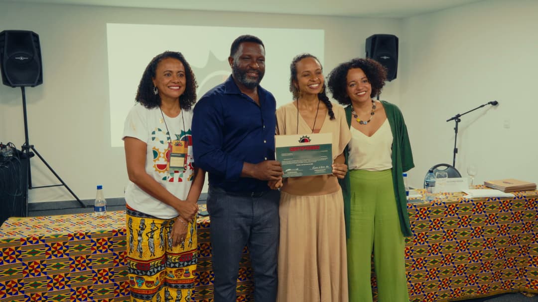 Quatro pessoas posam sorrindo diante da mesa; uma participante segura o certificado do programa.