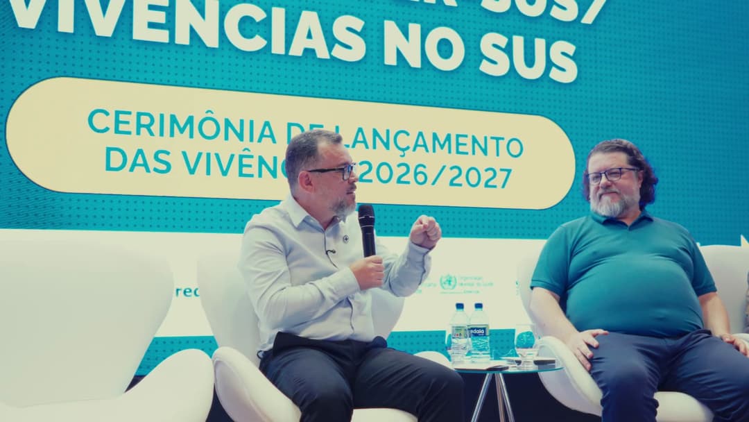 Frame do vídeo C7HkBSB2LtY Dois integrantes da mesa conversam sentados diante do painel da cerimônia de lançamento das Vivências 2026/2027.