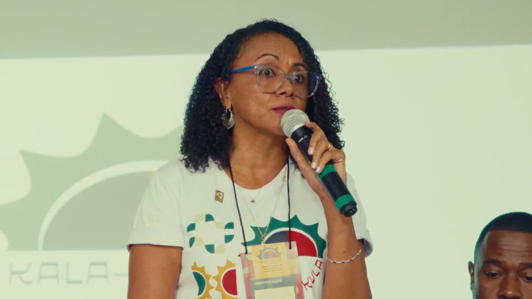 Frame do vídeo OJYjTONqukY Participante de óculos e camiseta do programa fala ao microfone.