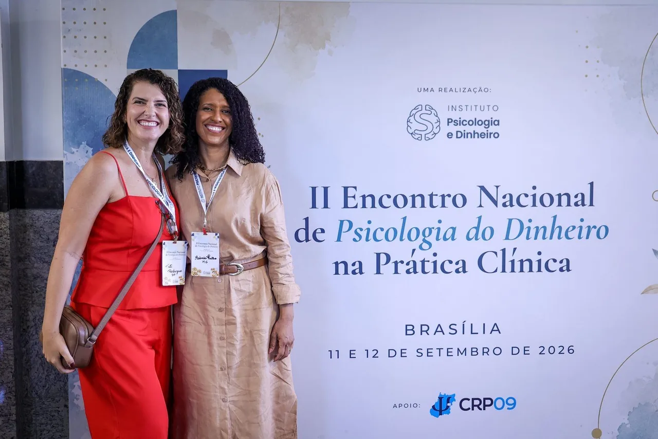 Duas participantes sorridentes diante do painel do II Encontro Nacional de Psicologia do Dinheiro na Prática Clínica