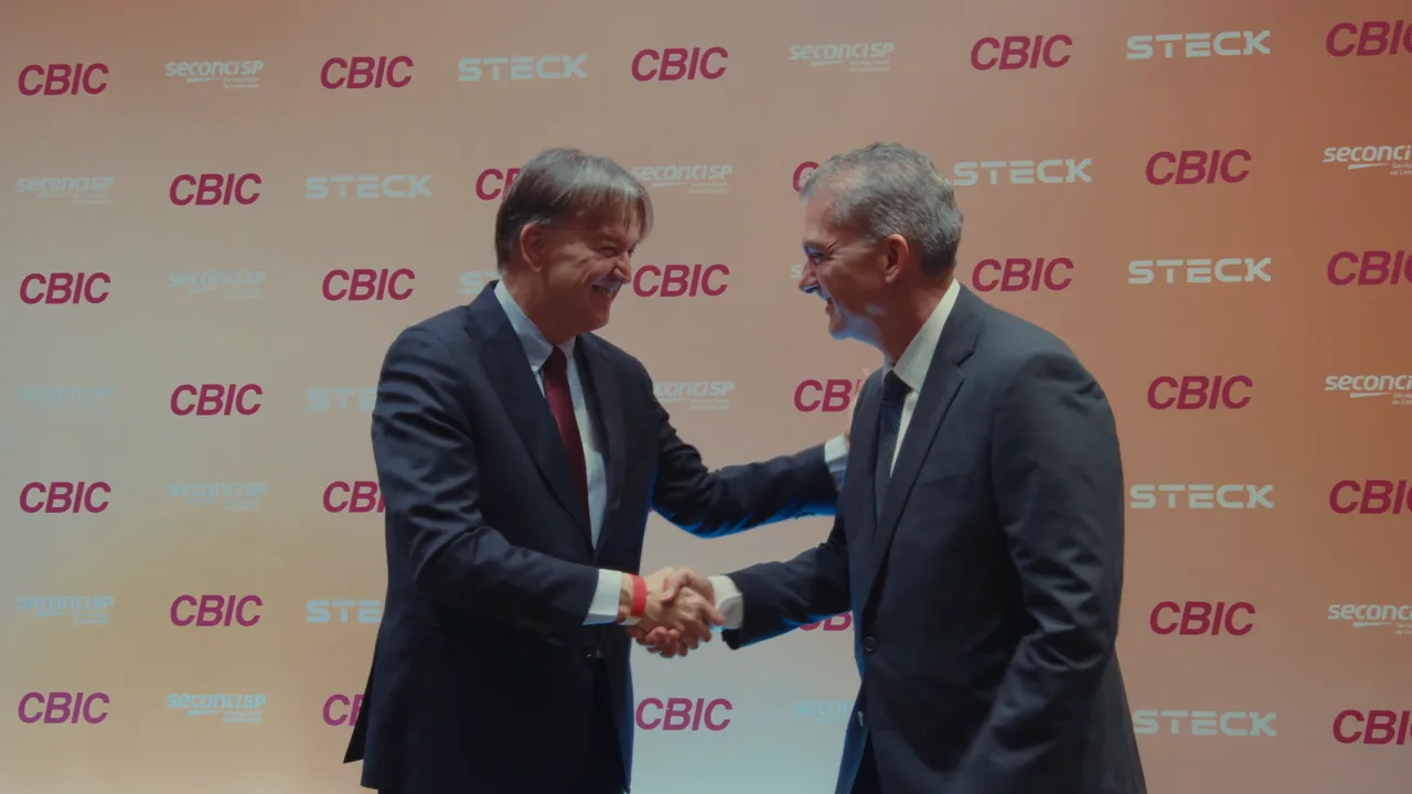 Dois homens de terno se cumprimentam diante do painel da CBIC, na cerimônia de posse da gestão 2026-2029